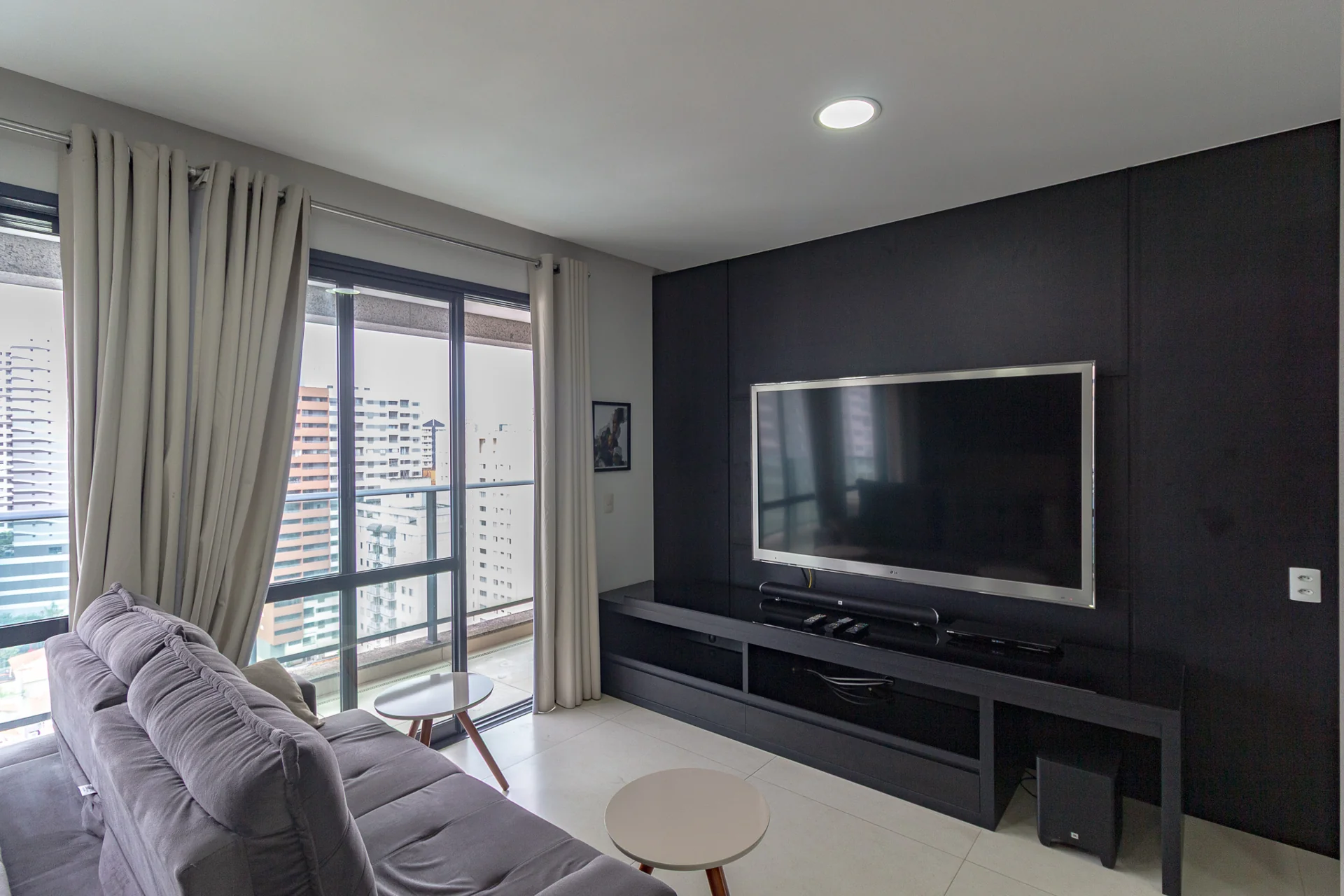 Sala de apartamento com painel de TV e janela ampla, vista do enquadramento usado na foto de capa